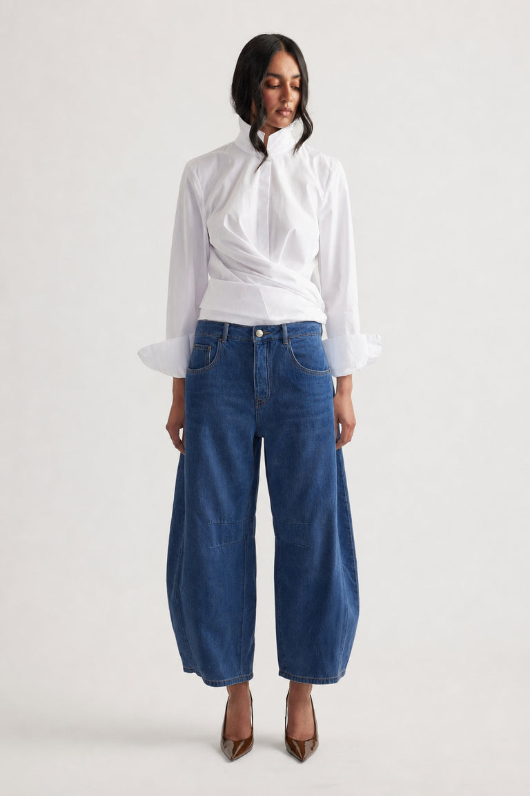 Woman wearing dark blue wide-leg jeans paired with a white long-sleeve blouse and brown pointed heels, front view