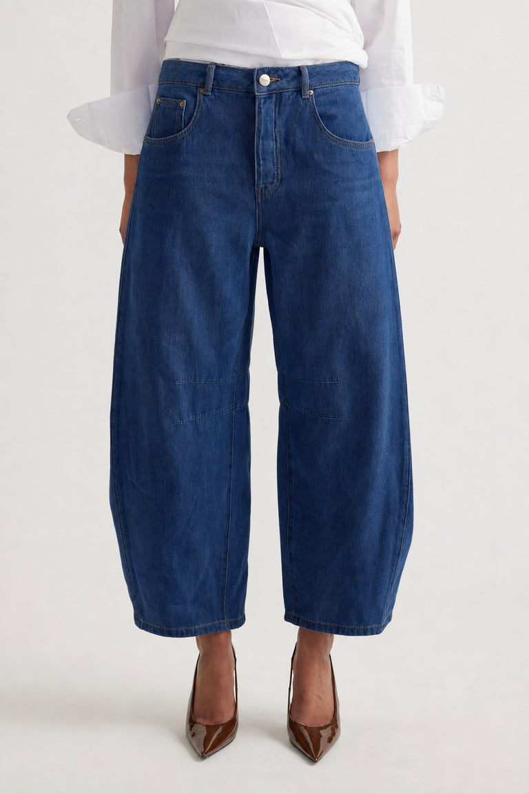 Wide-leg deep blue denim jeans with mid-rise waist and subtle seam details, styled with a white blouse and brown heels.