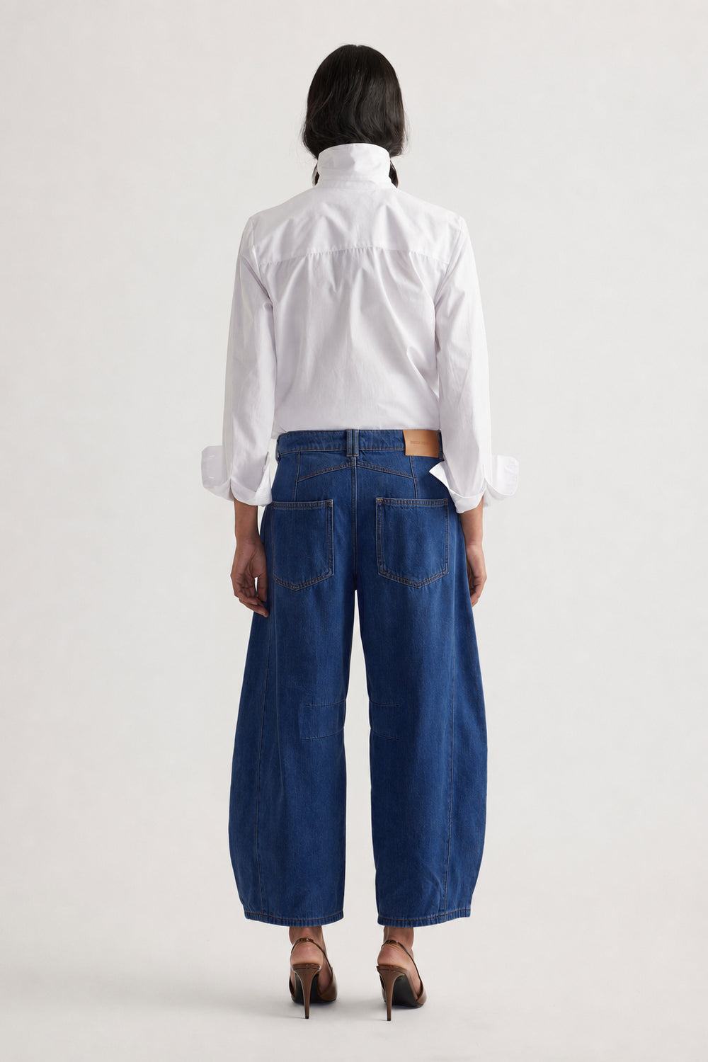 Woman seen from behind wearing wide-leg dark blue jeans paired with a crisp white shirt and heels