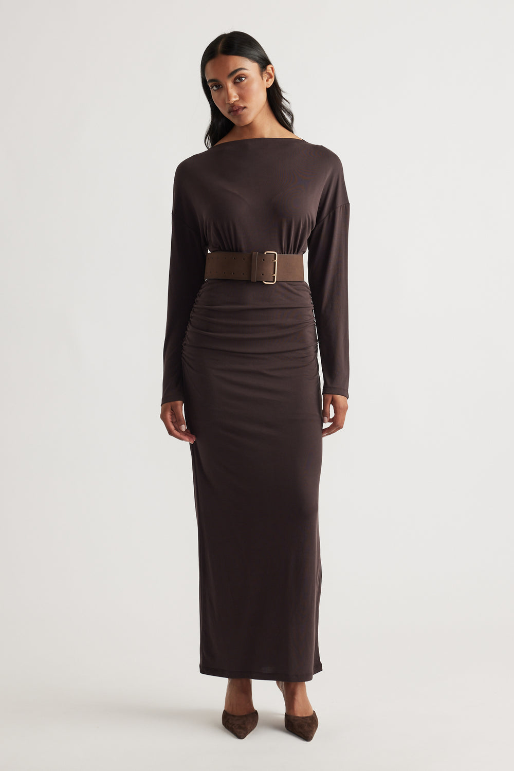 Woman wearing Tahlia Cinched Maxi Dress in rich cedar brown with long sleeves, boat neckline, cinched waist, and paired with matching belt and pointed shoes