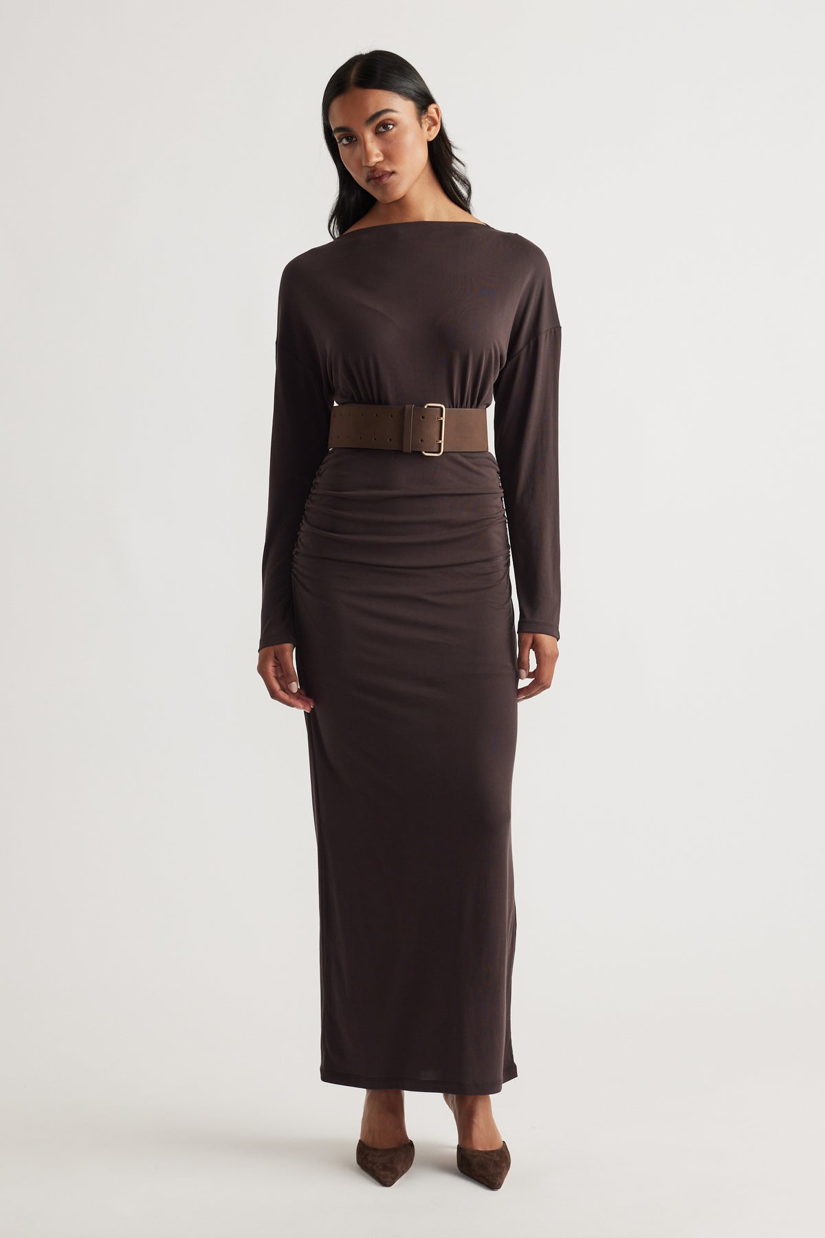 Woman wearing Tahlia Cinched Maxi Dress in rich cedar brown with long sleeves, boat neckline, cinched waist, and paired with matching belt and pointed shoes
