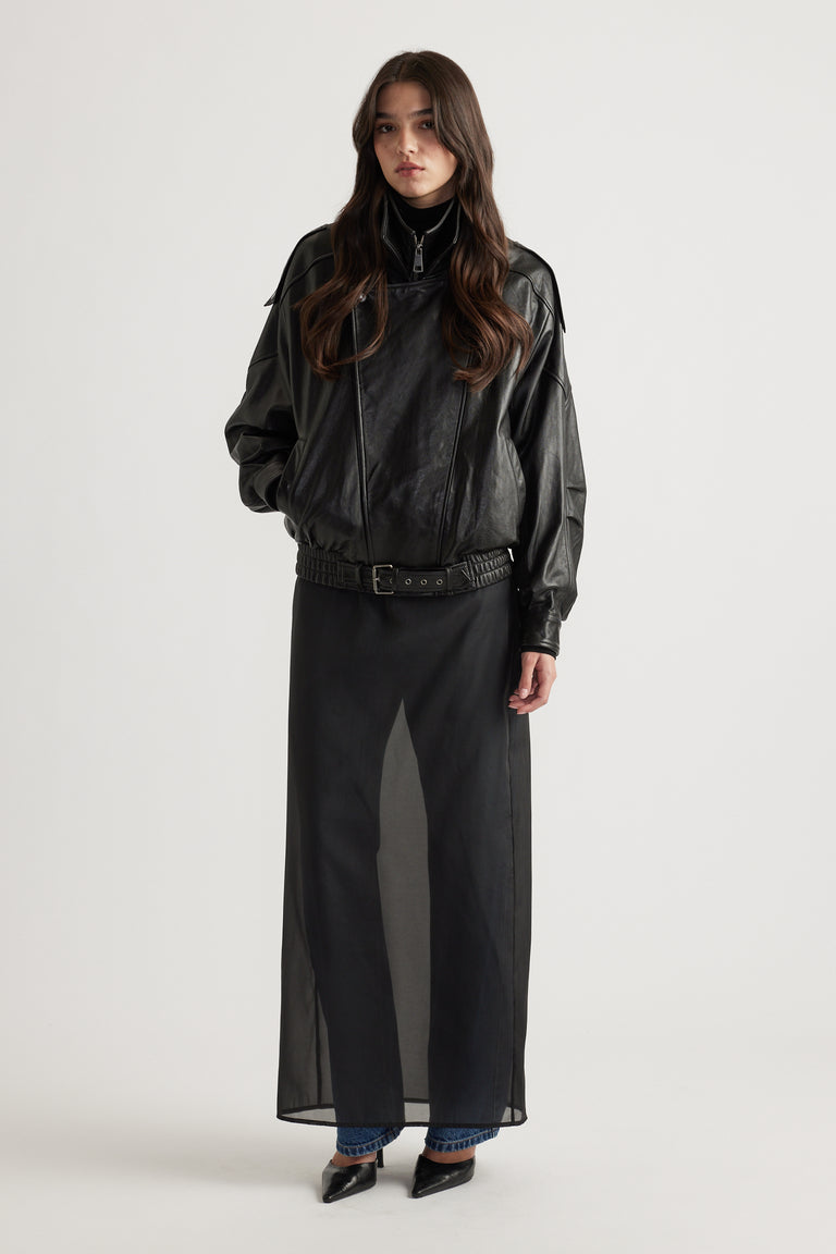 Young woman wearing an oversized black leather jacket layered over sheer black skirt and blue jeans with pointed black heels