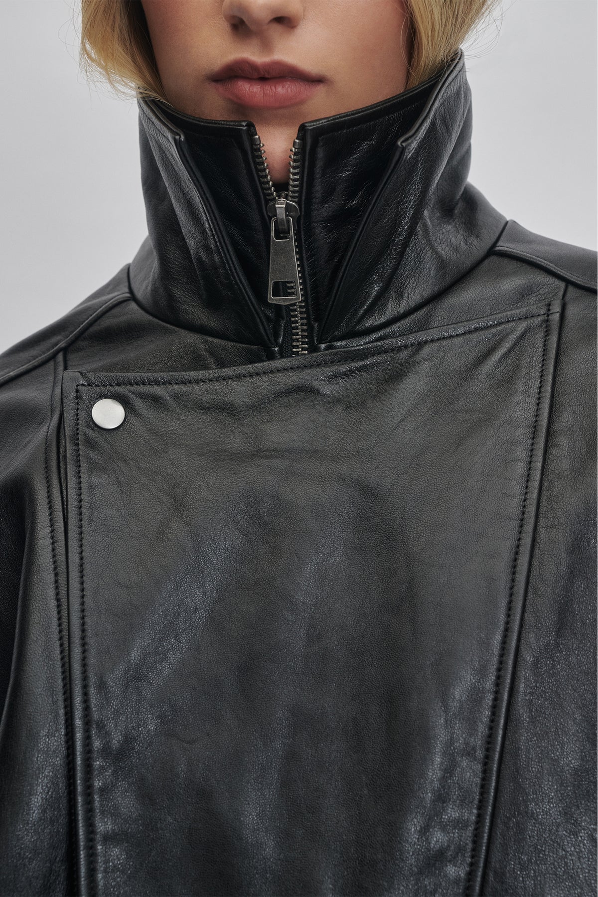 Close-up of black leather jacket with high collar and exposed silver zipper for a sleek, modern look