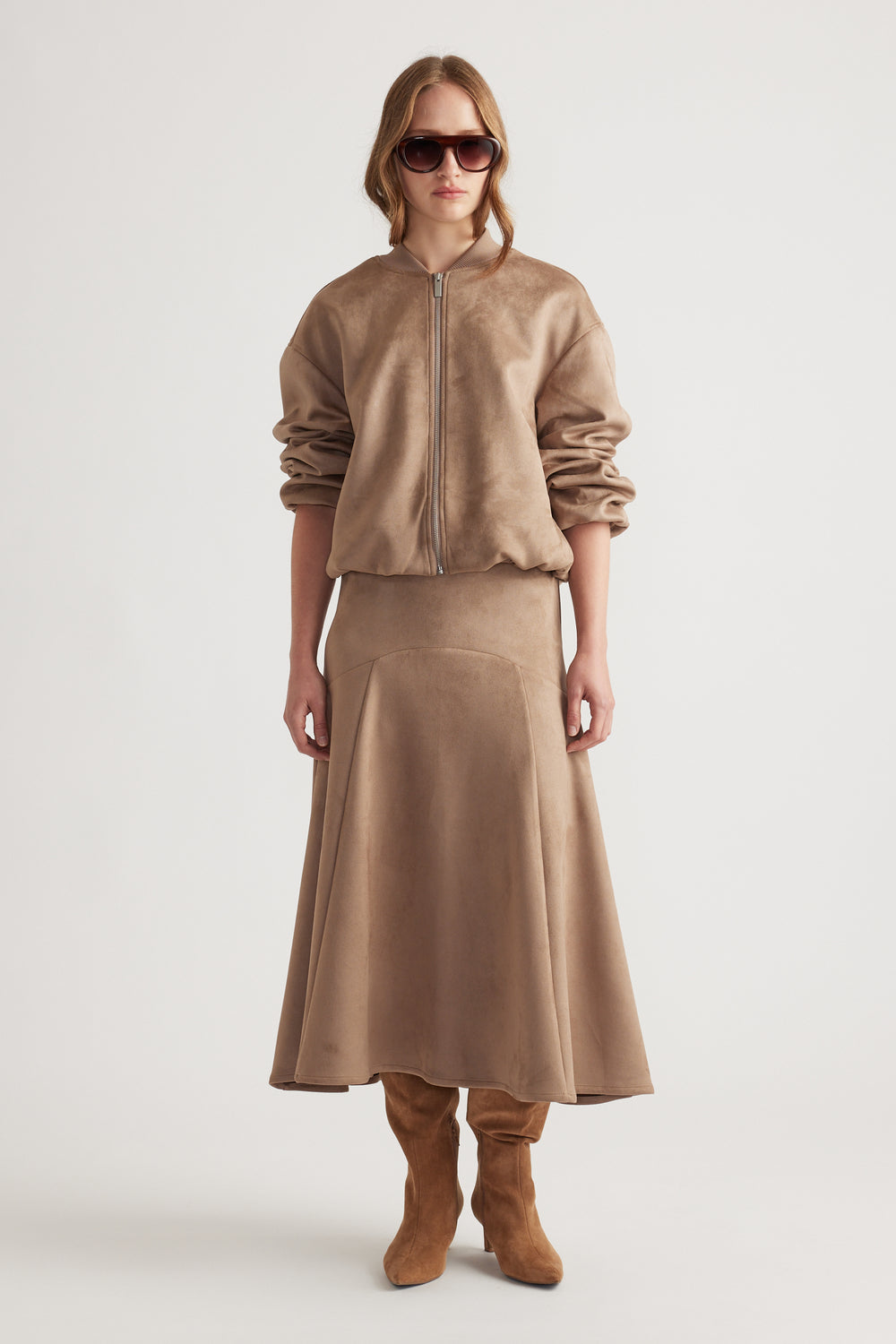 Model wearing a soft dove grey faux suede midi skirt with matching zip-up jacket and suede knee-high boots