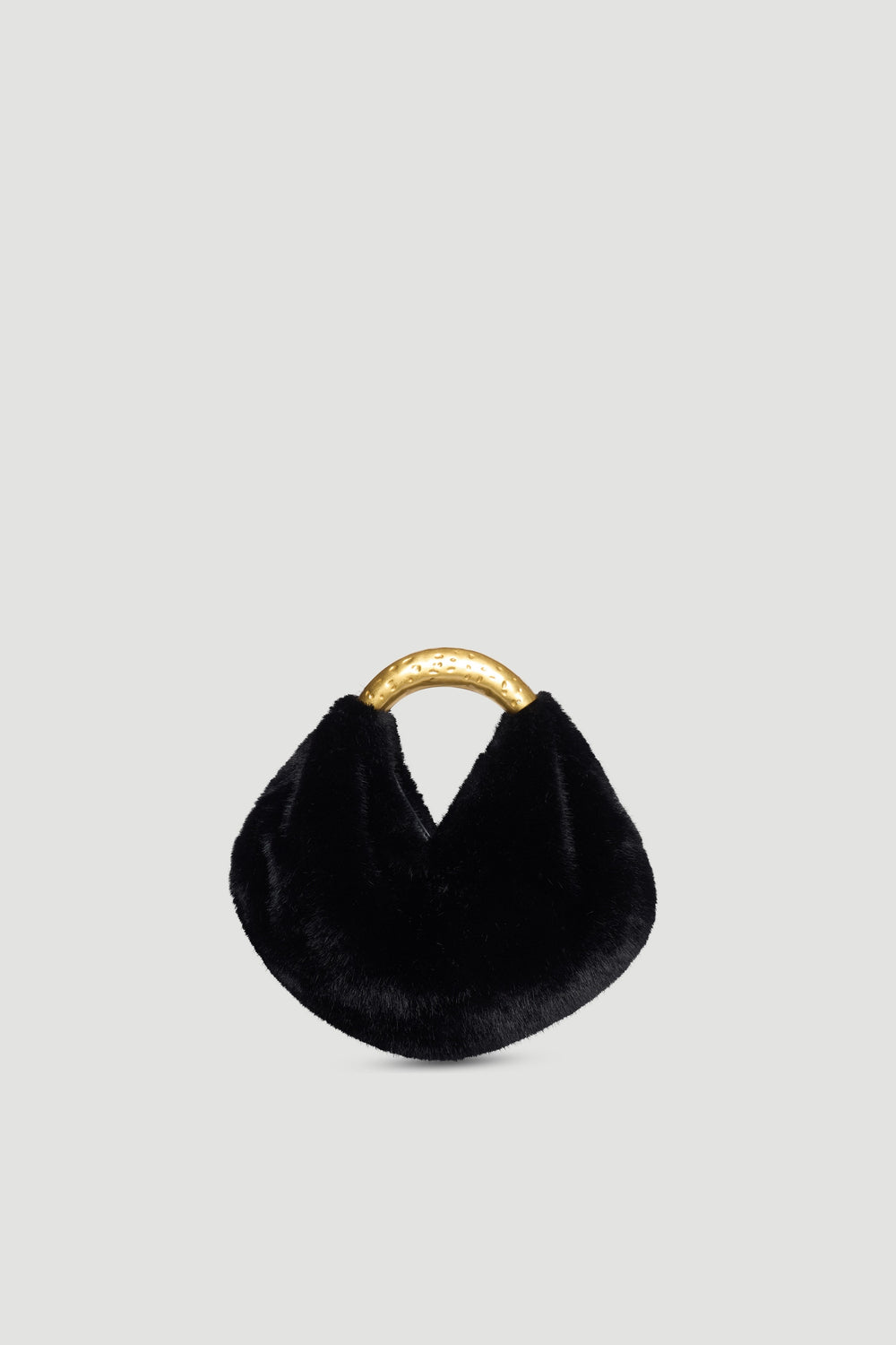 Small black faux fur bag with curved hammered gold metal handle and magnetic snap closure on plain background