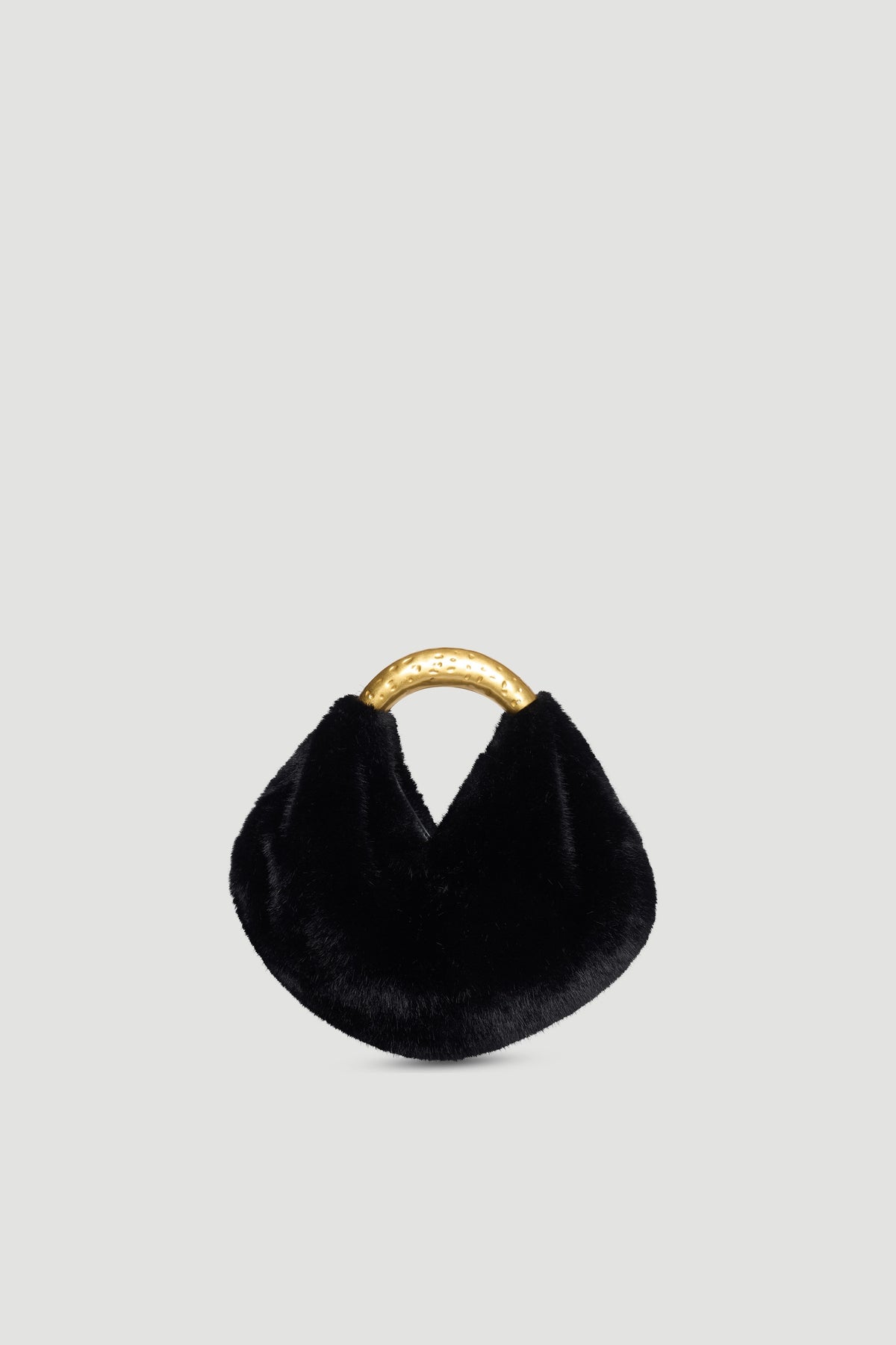 Small black faux fur bag with curved hammered gold metal handle and magnetic snap closure on plain background