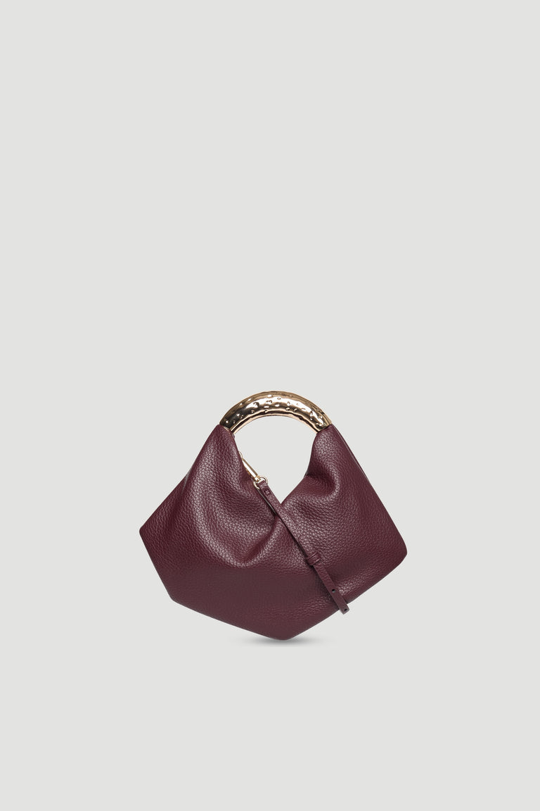 Small deep burgundy bag with soft pebble texture and distinctive hammered metal handle on light background