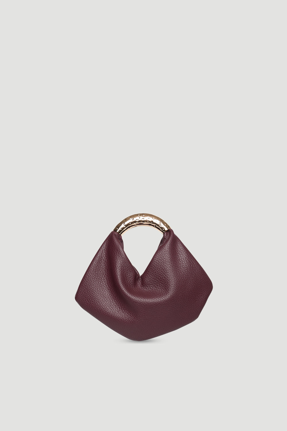 Small soft pebble bag in deep burgundy with hammered gold metal handle and magnetic snap closure against neutral background