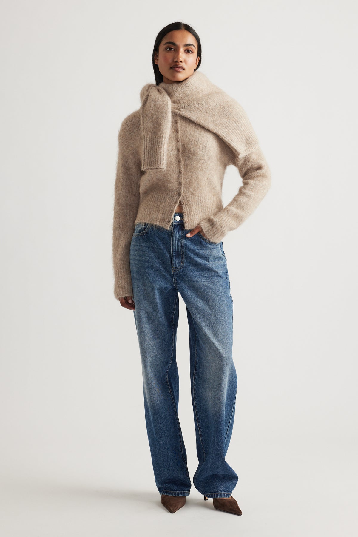 Woman wearing a soft beige alpaca blend cardigan layered with a matching scarf, paired with relaxed blue denim jeans.