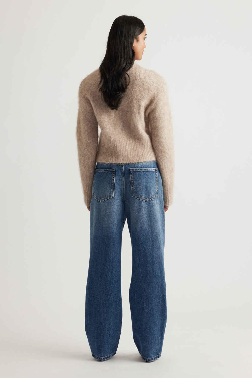 Rear view of woman wearing a soft beige alpaca blend cardigan paired with relaxed fit blue denim jeans