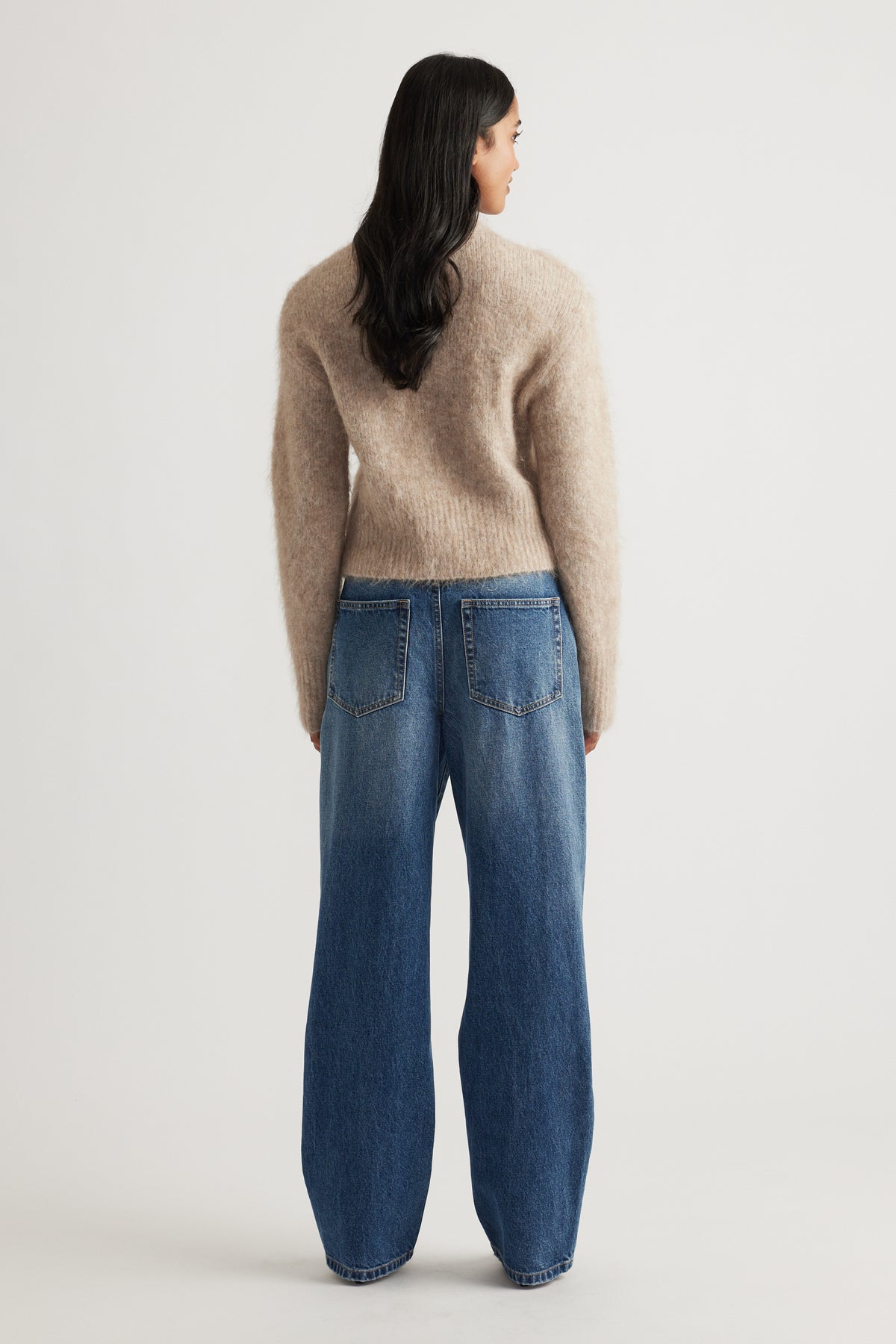Rear view of woman wearing a soft beige alpaca blend cardigan paired with relaxed fit blue denim jeans