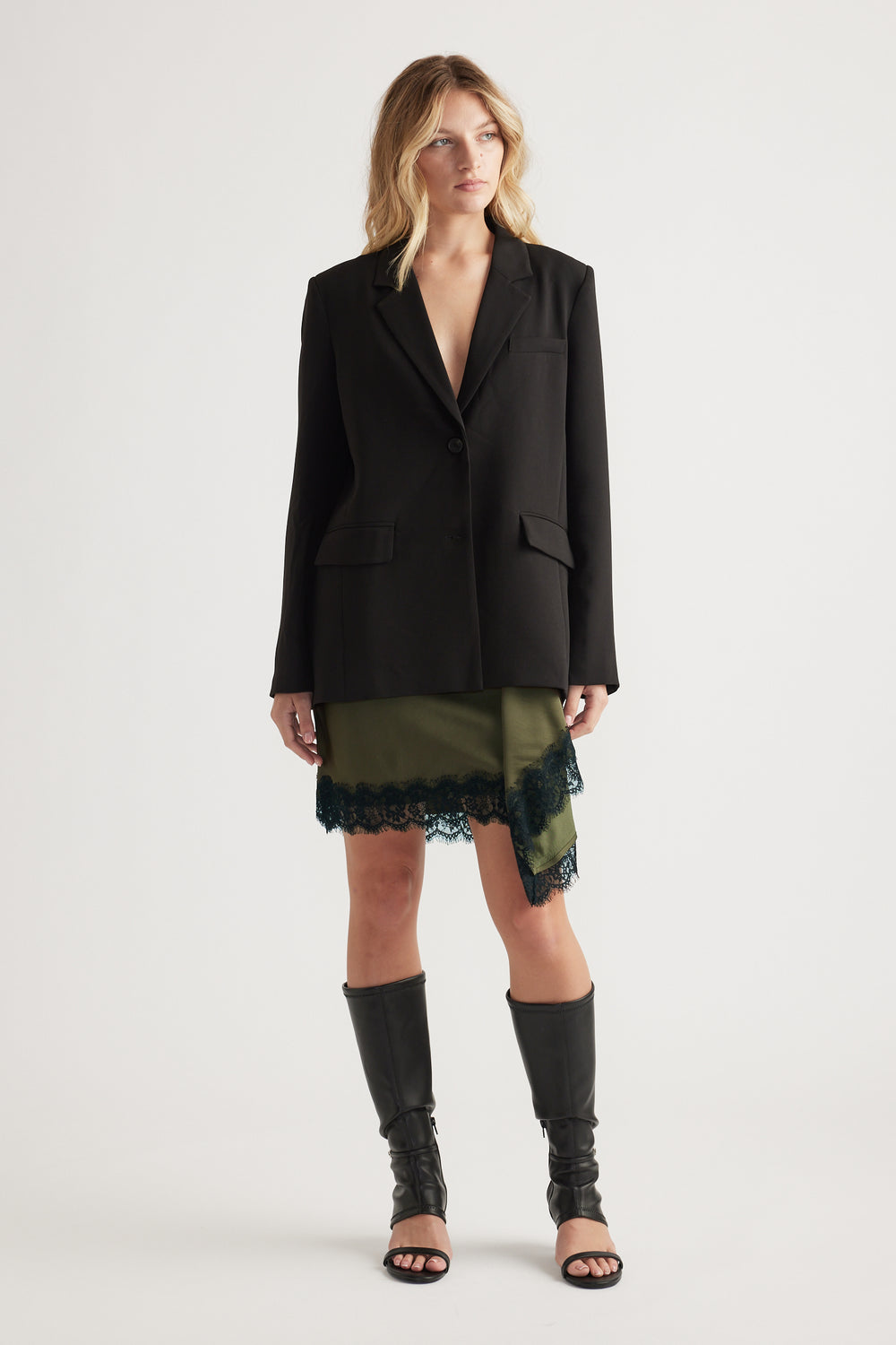 Woman wearing an olive mini skirt with black lace trim paired with a black blazer and knee-high open-toe boots
