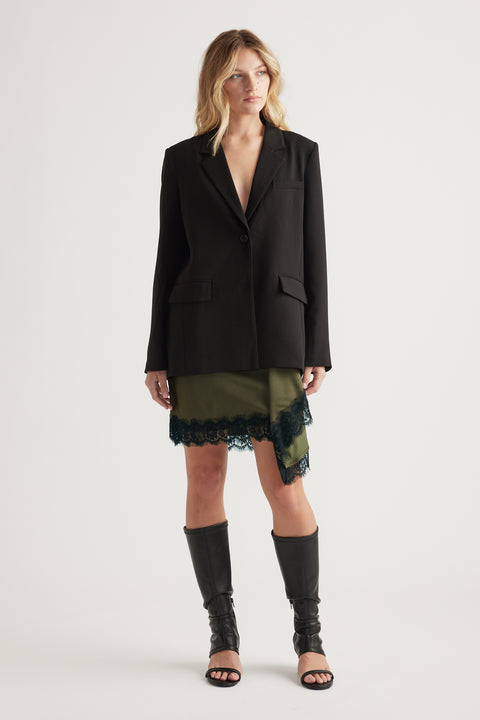 Woman wearing an olive mini skirt with black lace trim paired with a black blazer and knee-high open-toe boots