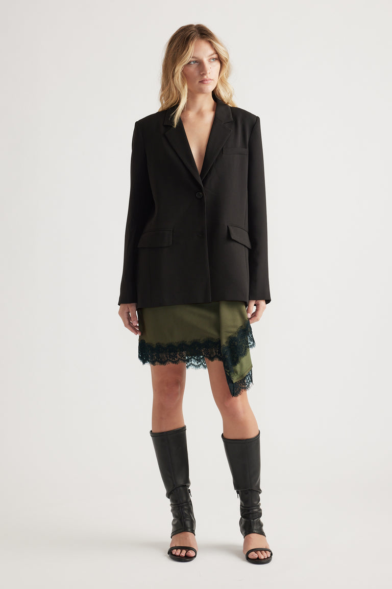 Woman wearing an olive mini skirt with black lace trim paired with a black blazer and knee-high open-toe boots