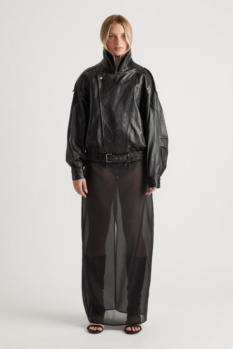 Woman wearing a black belted leather jacket paired with a sheer black maxi skirt and black open-toe heels