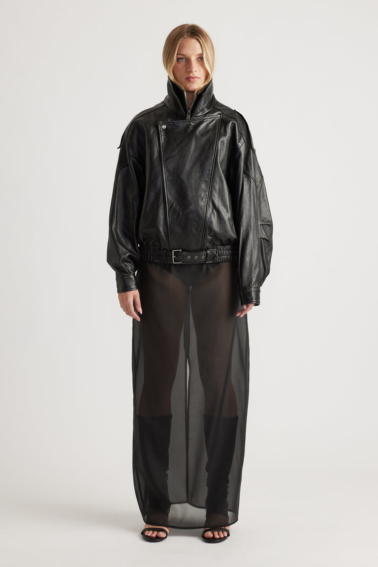 Woman wearing a black belted leather jacket paired with a sheer black maxi skirt and black open-toe heels