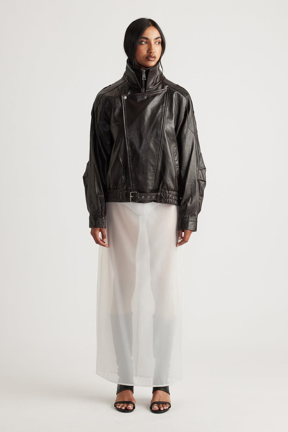 Woman wearing a black leather jacket layered over a sheer ivory maxi skirt with black open-toe heels for a contemporary look