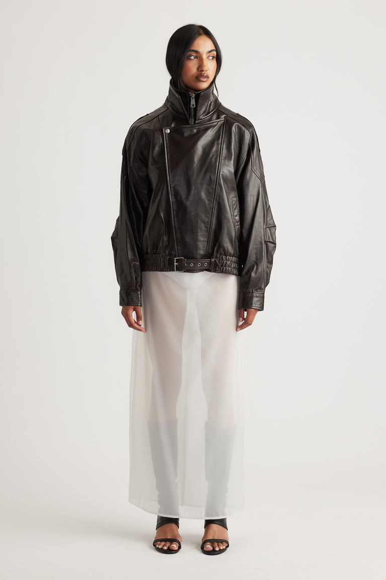 Woman wearing a black leather jacket layered over a sheer ivory maxi skirt with black open-toe heels for a contemporary look