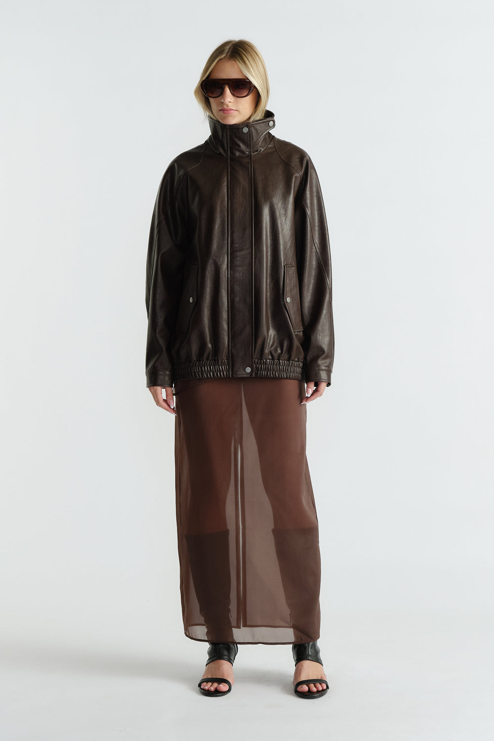 Woman wearing a dark brown leather jacket paired with a sheer brown maxi skirt and black open-toe heels