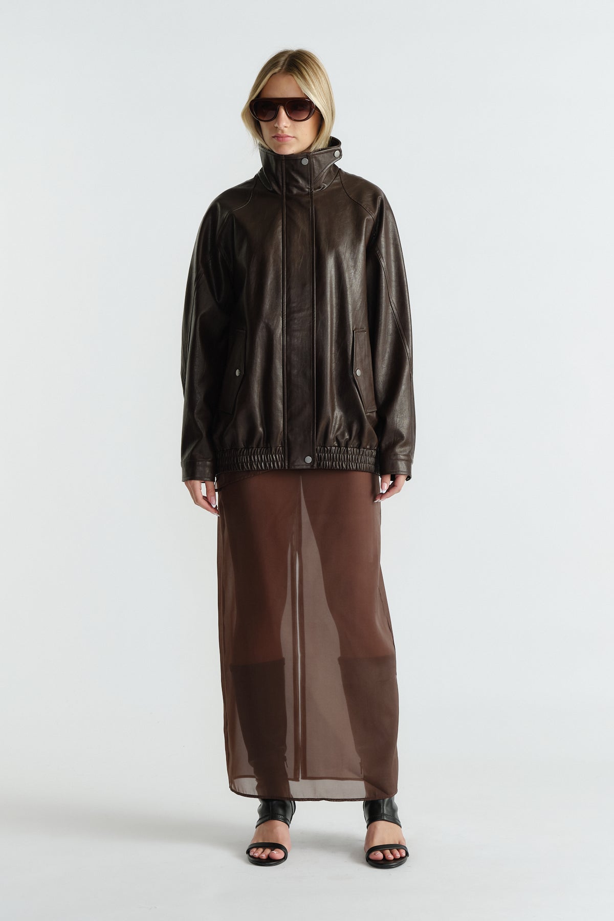 Woman wearing a dark brown leather jacket paired with a sheer brown maxi skirt and black open-toe heels
