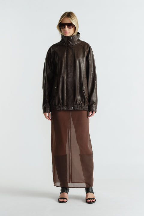 Woman wearing a dark brown leather jacket paired with a sheer brown maxi skirt and black open-toe heels