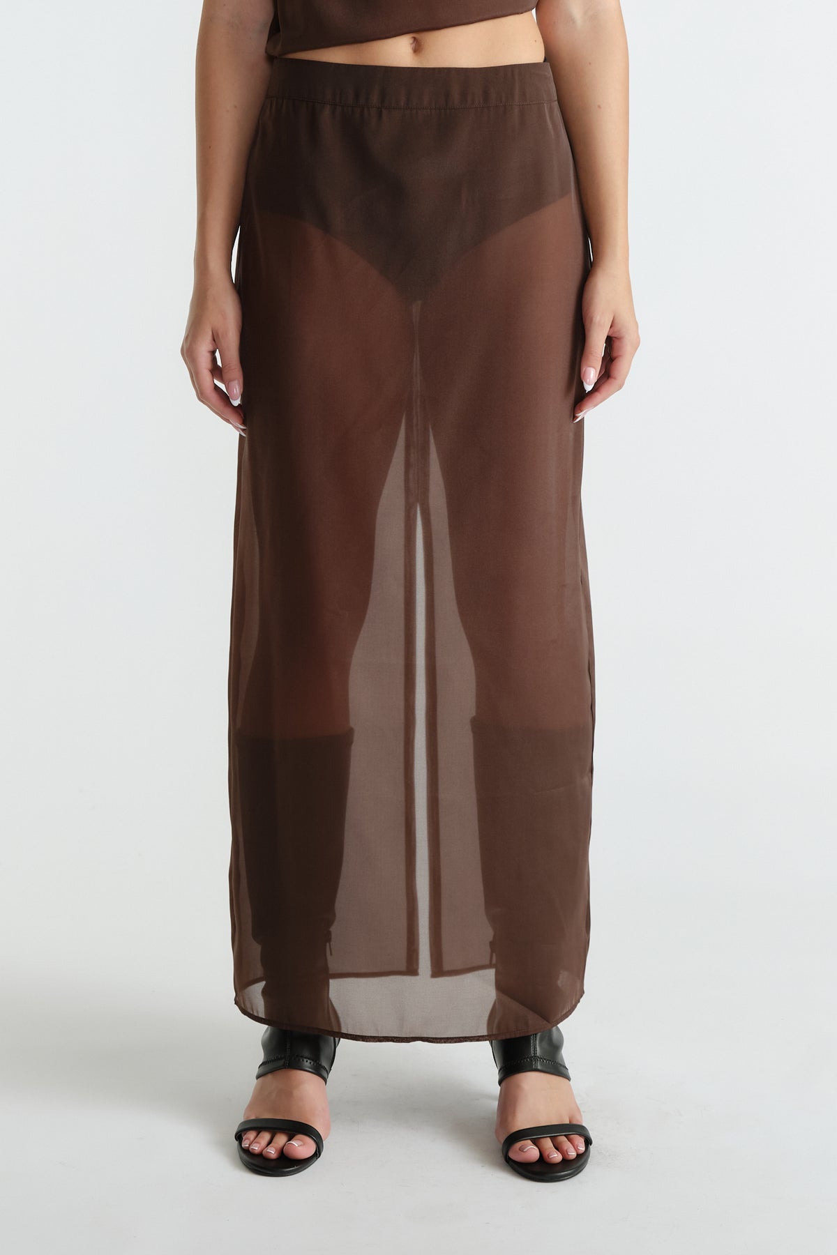 Front view of woman wearing sheer brown maxi skirt with back slit paired with black open-toe heels