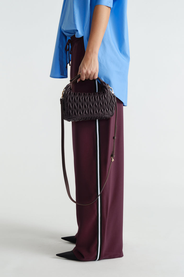 Side view of woven burgundy bag with top handle and long strap, paired with relaxed pants and blue top