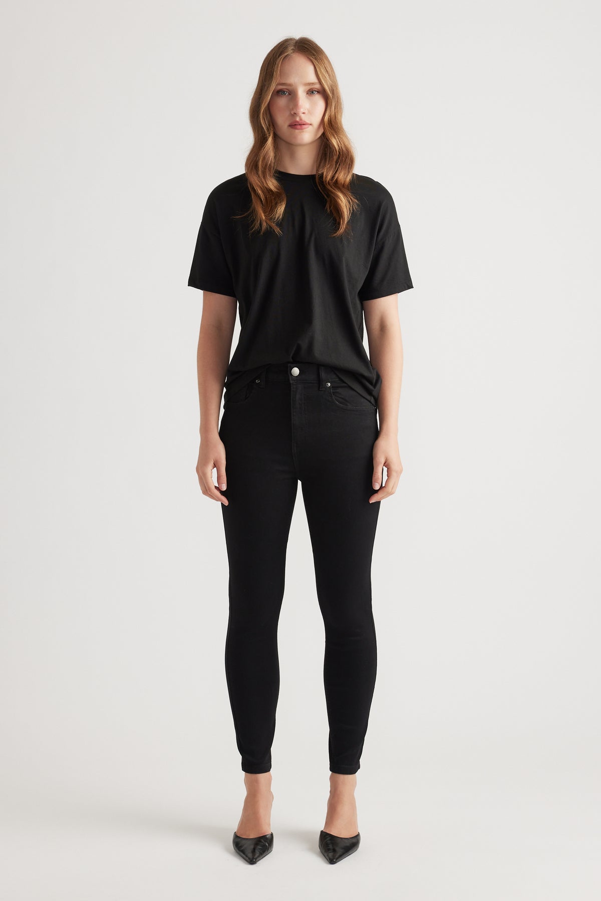 Woman wearing black skinny denim jeans paired with a relaxed black tee and pointed black heels for a sleek look