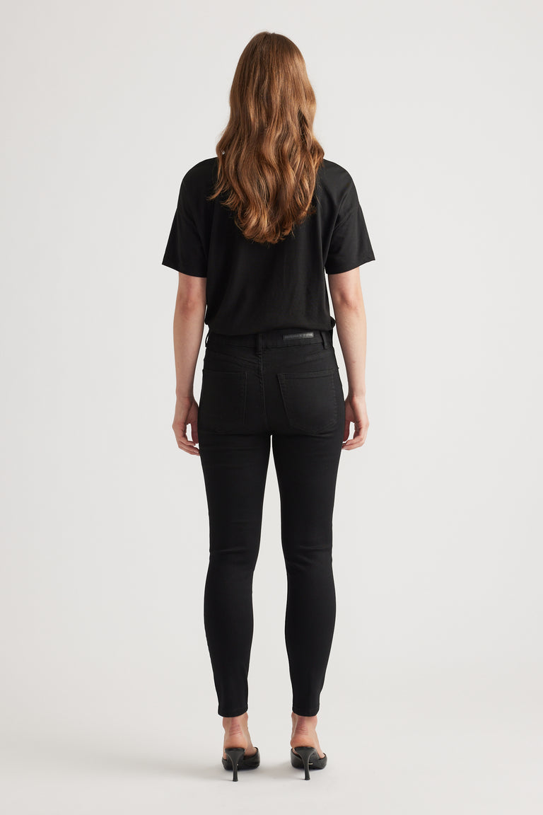 Back view of a woman wearing slim black skinny jeans paired with a simple black short-sleeve top and heels.