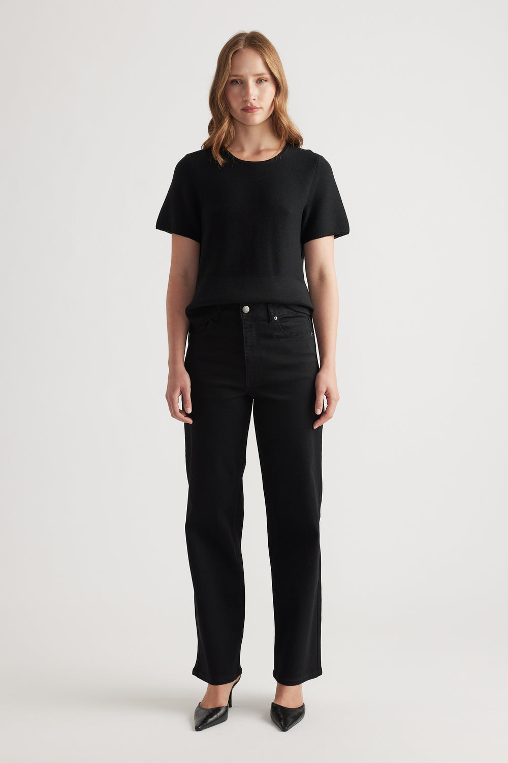 Woman wearing black stretch straight jeans paired with a simple black short-sleeve knit top and pointed heels