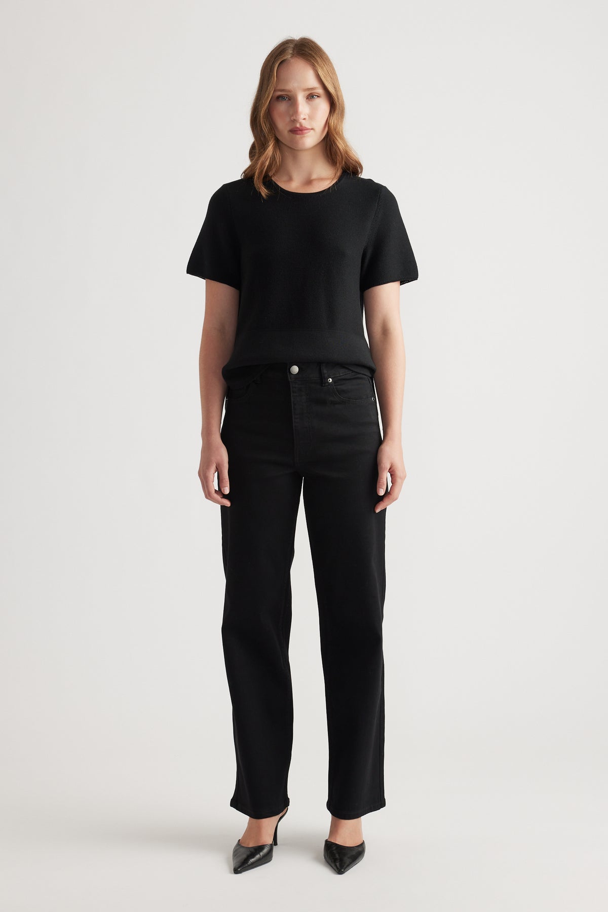 Woman wearing black stretch straight jeans paired with a simple black short-sleeve knit top and pointed heels