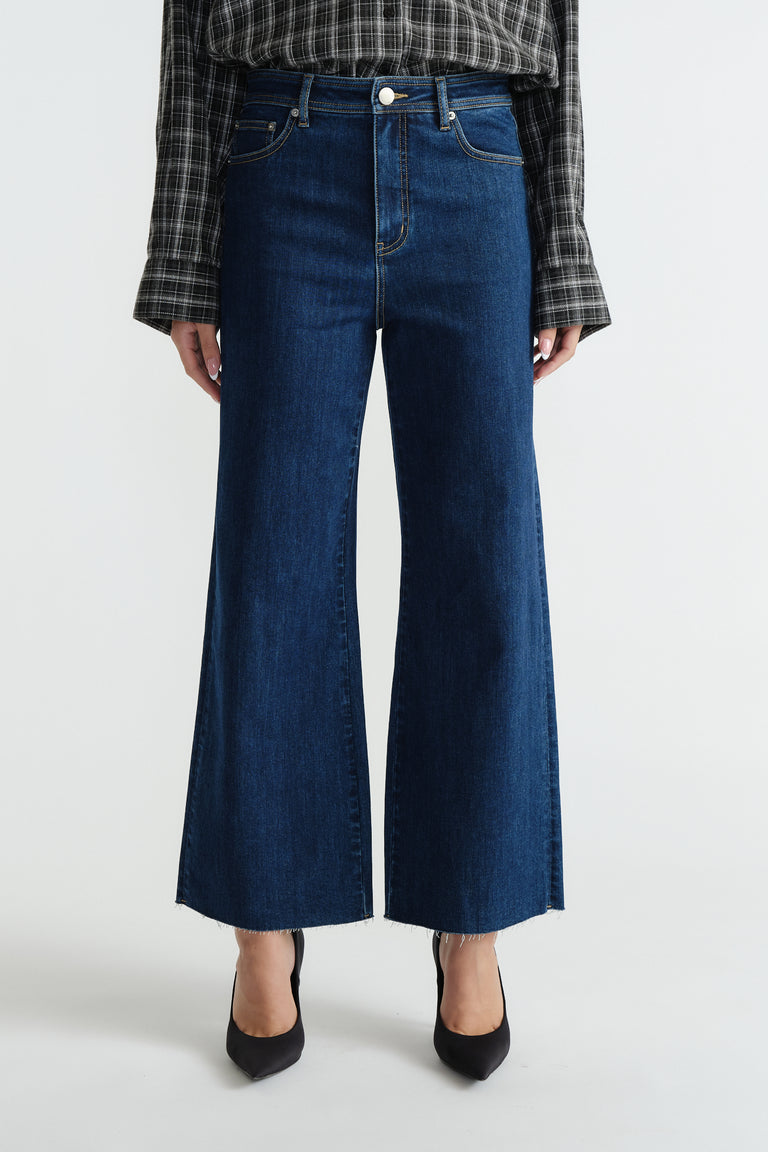 Dark indigo wide-leg jeans styled with a relaxed fit, paired with a casual plaid shirt and black heels.