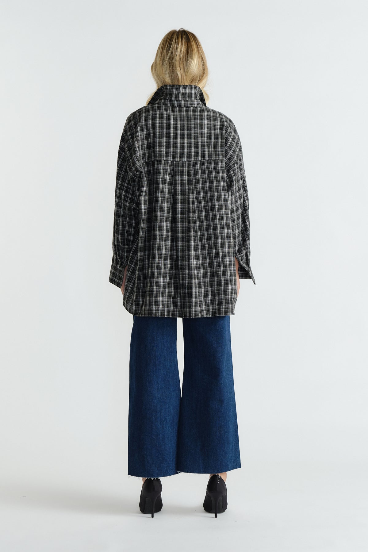 Woman wearing dark indigo wide-leg denim jeans paired with a loose, black and white checkered jacket and black heeled shoes