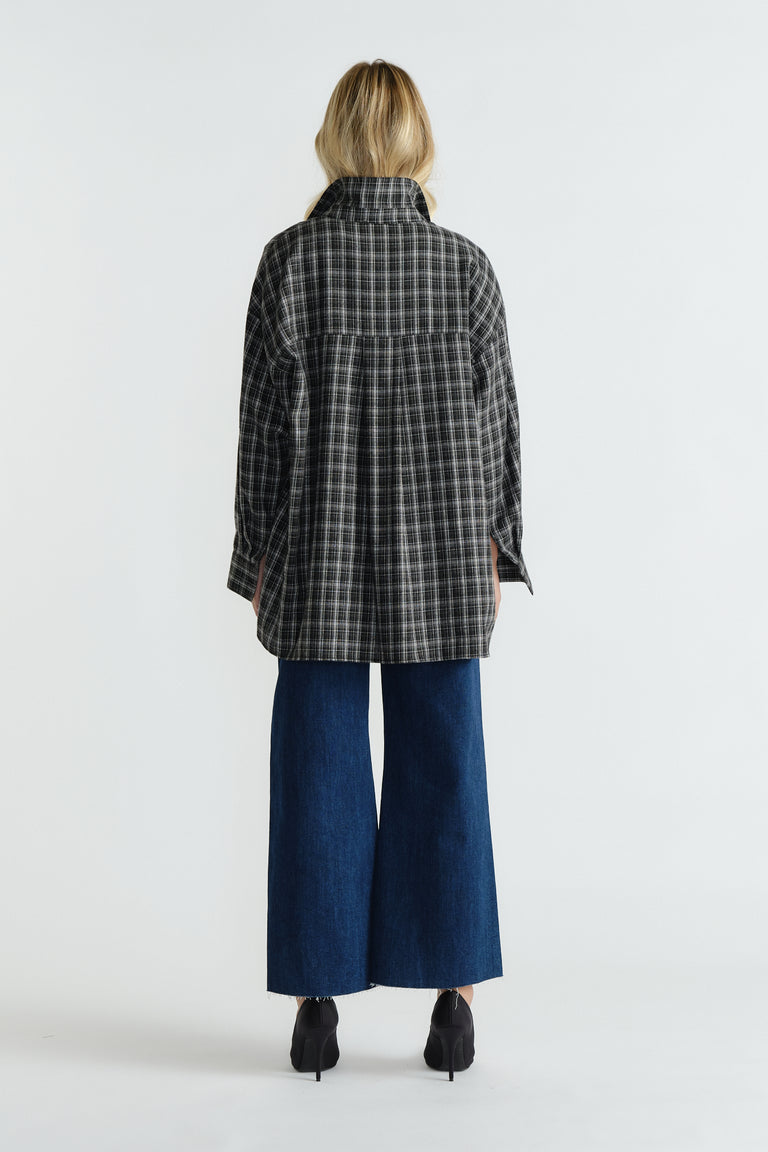 Woman wearing dark indigo wide-leg denim jeans paired with a loose, black and white checkered jacket and black heeled shoes
