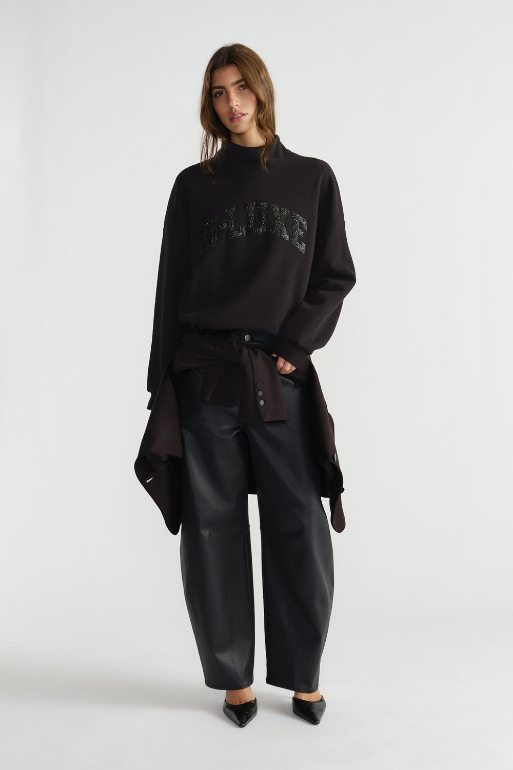 Woman wearing a relaxed black mock neck sweat with subtle sparkle detail, styled with loose black trousers and pointed shoes.