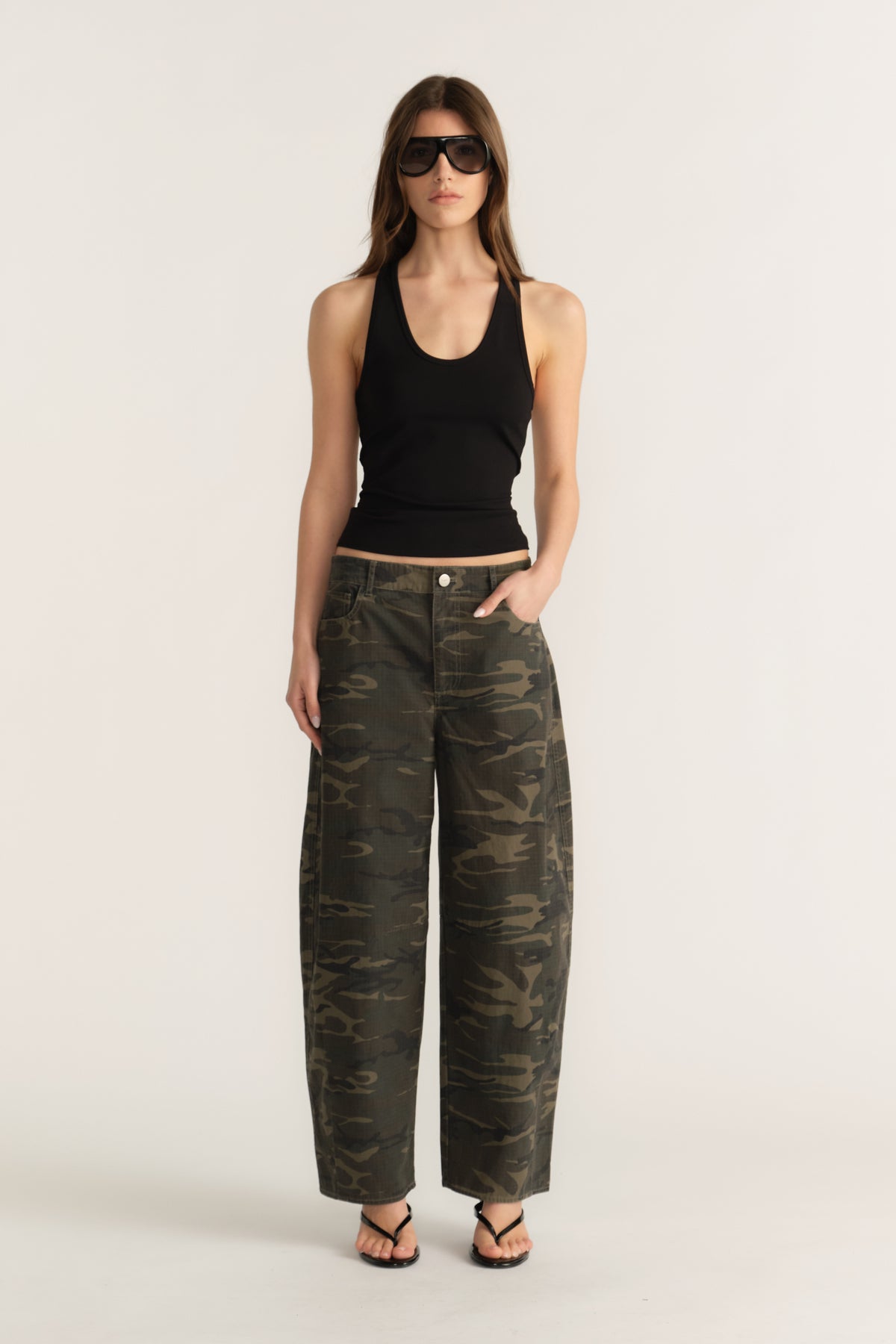 Model wearing camo barrel-leg pants with a mid-rise waist, styled with a black tank top and sunglasses