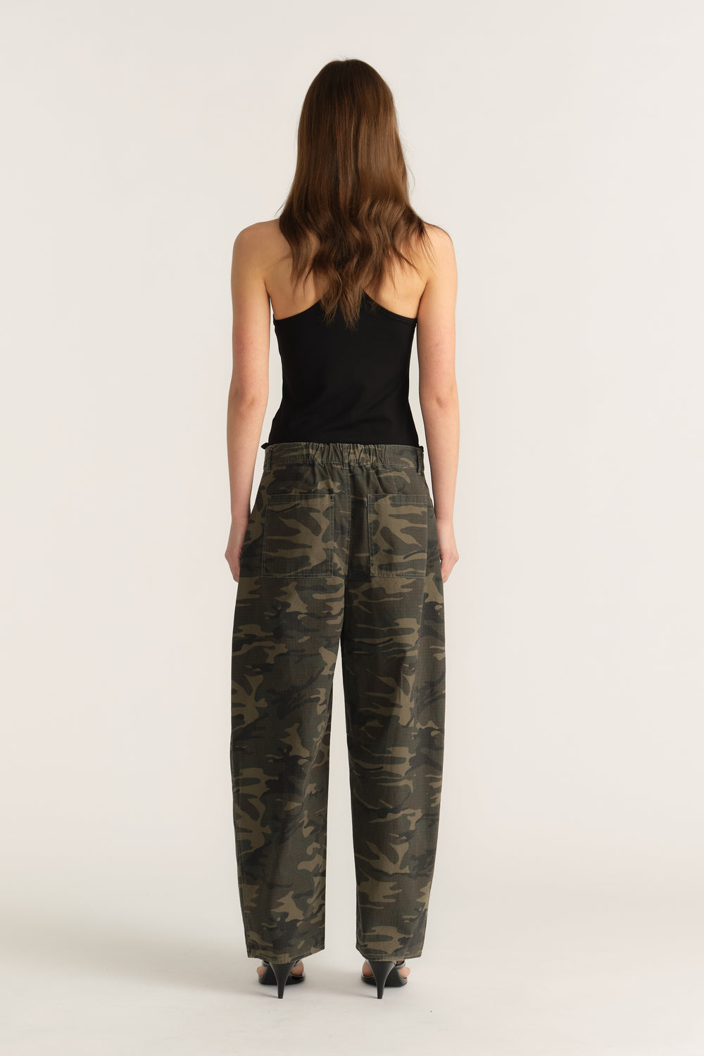 Back view of woman wearing a black tank top with mid-rise camo barrel-leg pants