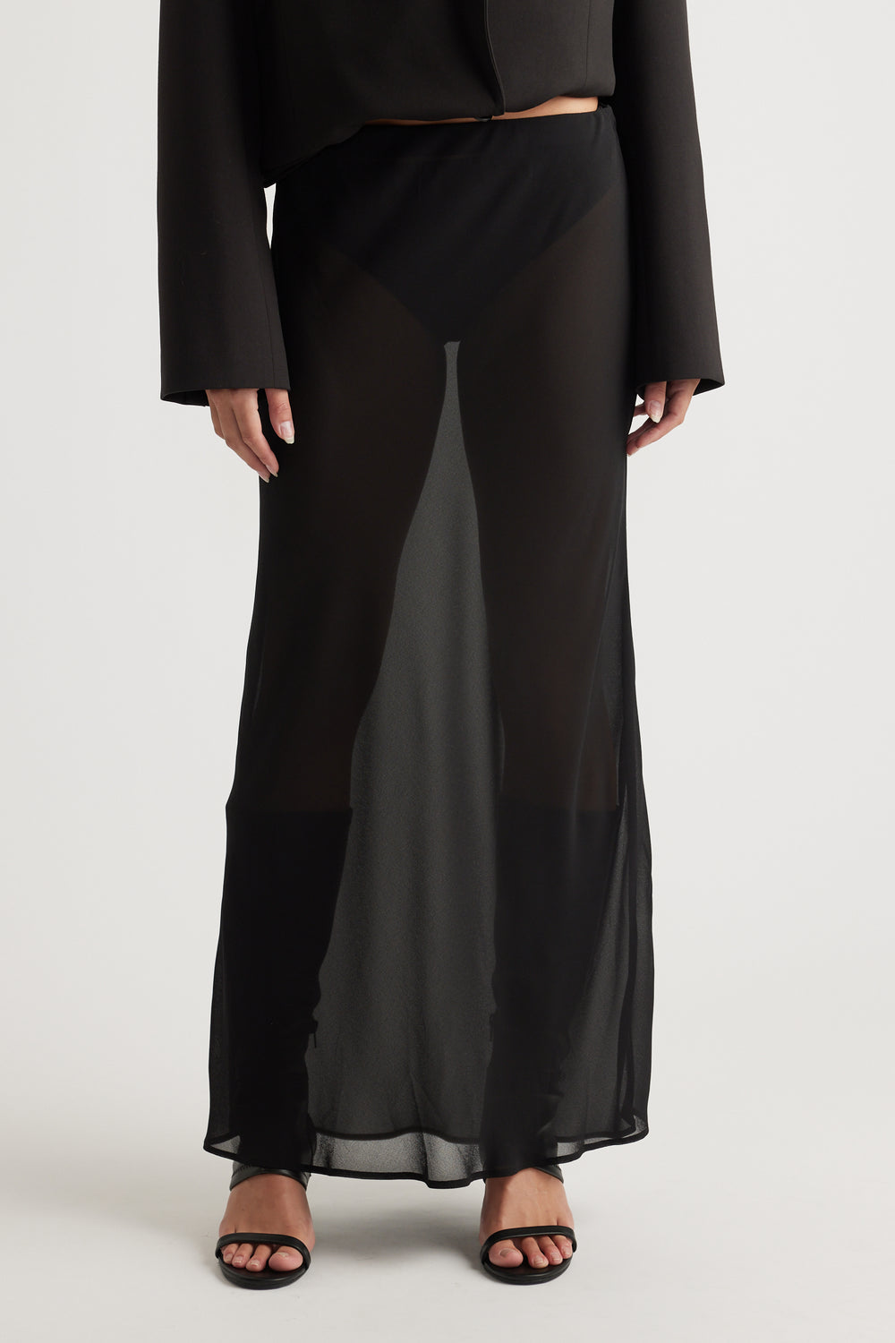 Woman styling Faye Sheer Maxi Skirt in black layered over black shorts with open-toe heels by DECJUBA Australian fashion label