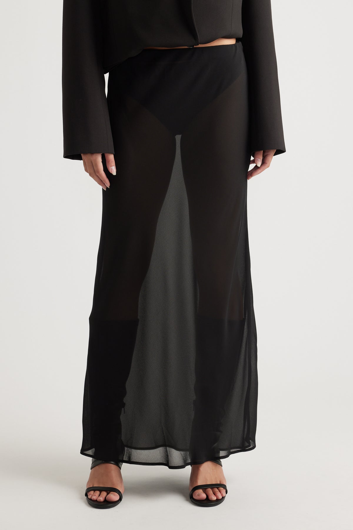 Woman styling Faye Sheer Maxi Skirt in black layered over black shorts with open-toe heels by DECJUBA Australian fashion label