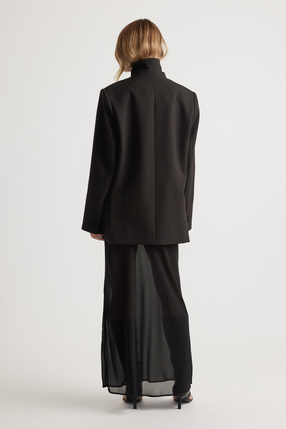 Woman wearing Faye Sheer Maxi Skirt in black layered under tailored black blazer by DECJUBA Australian fashion brand