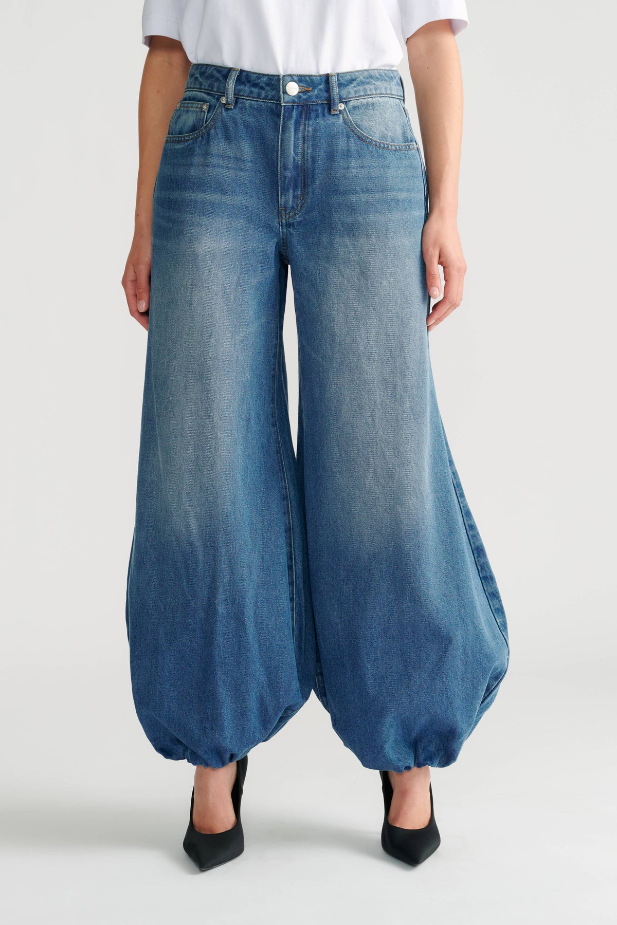 Woman wearing medium wash high-rise balloon jeans with gathered hems paired with black pointed heels.