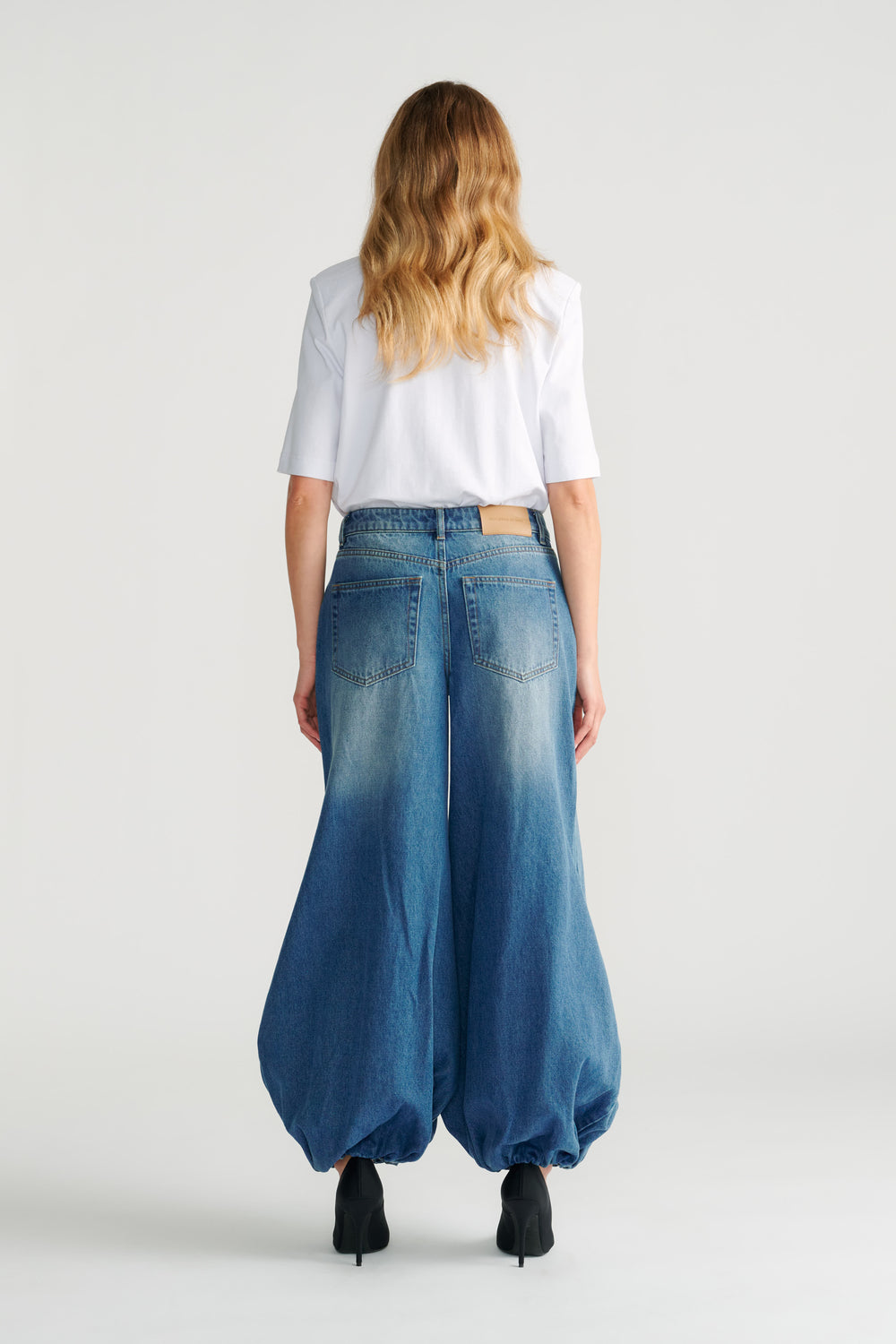 Woman wearing relaxed high-rise balloon denim jeans in faded blue with a white short sleeve top and black heels.