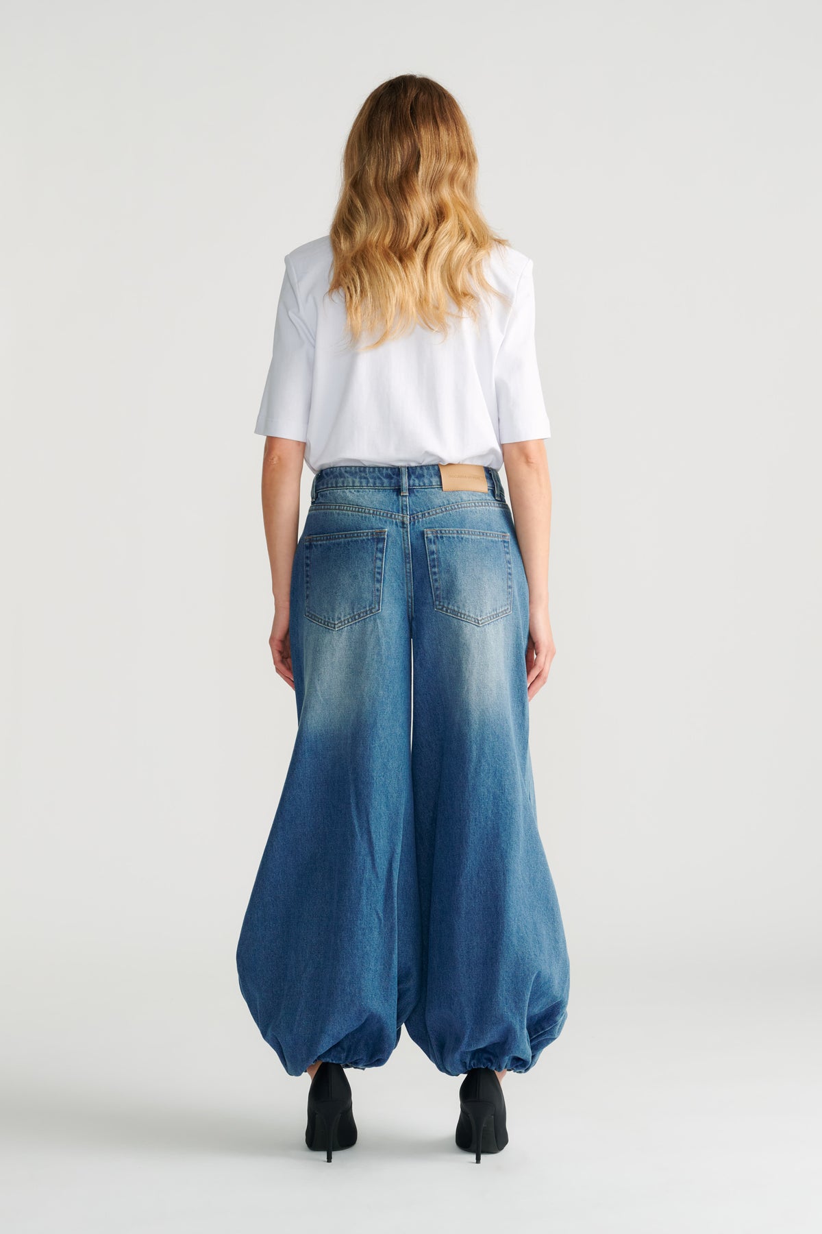 Woman wearing relaxed high-rise balloon denim jeans in faded blue with a white short sleeve top and black heels.