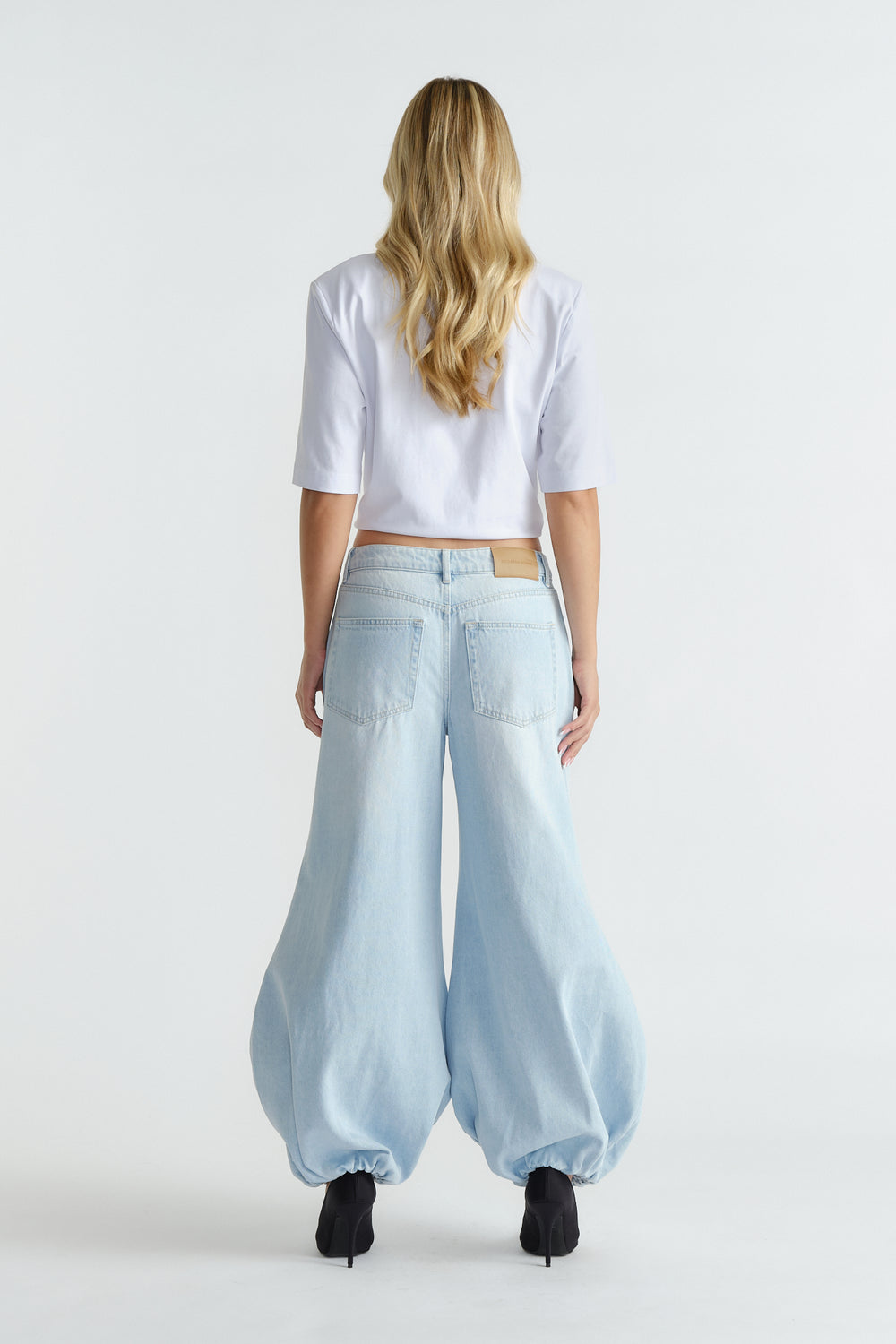 Woman seen from behind wearing light blue high-rise balloon jeans with gathered hems and black heels.