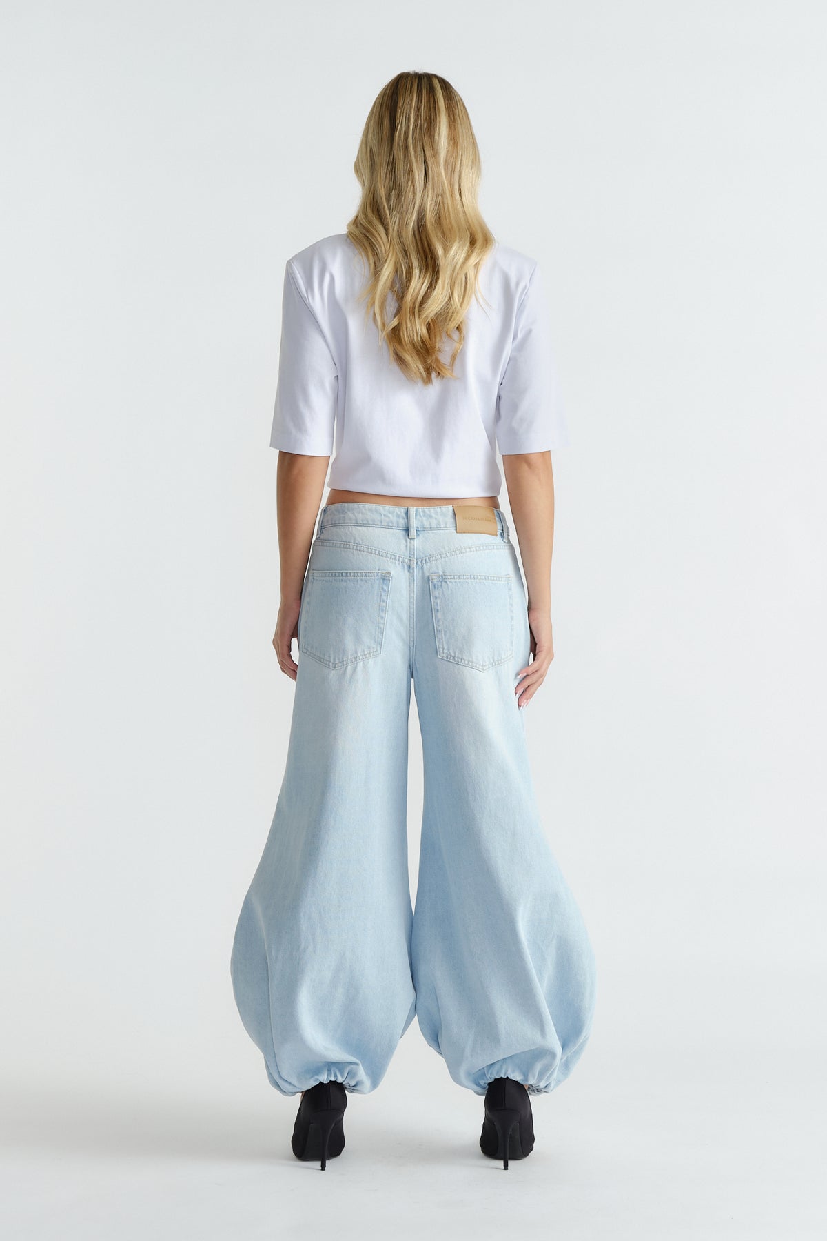 Woman seen from behind wearing light blue high-rise balloon jeans with gathered hems and black heels.