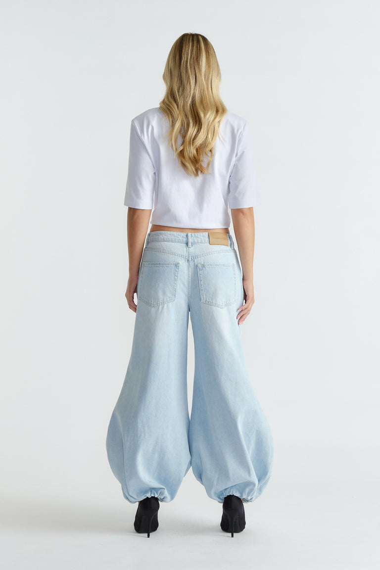 Woman seen from behind wearing light blue high-rise balloon jeans with gathered hems and black heels.