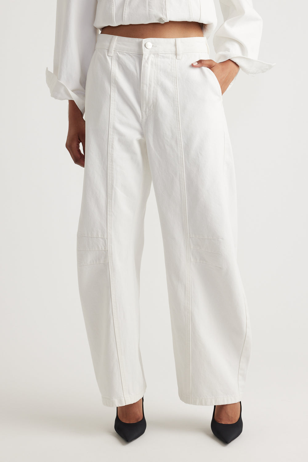 Person wearing white barrel jeans and a white top on a plain background