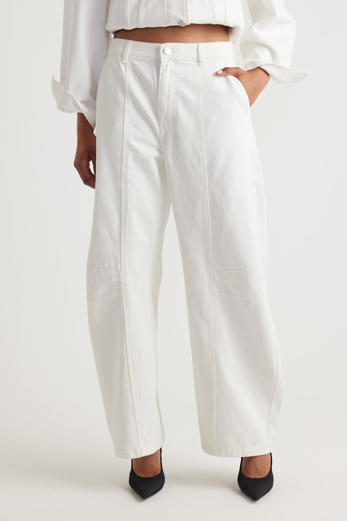 Person wearing white barrel jeans and a white top on a plain background