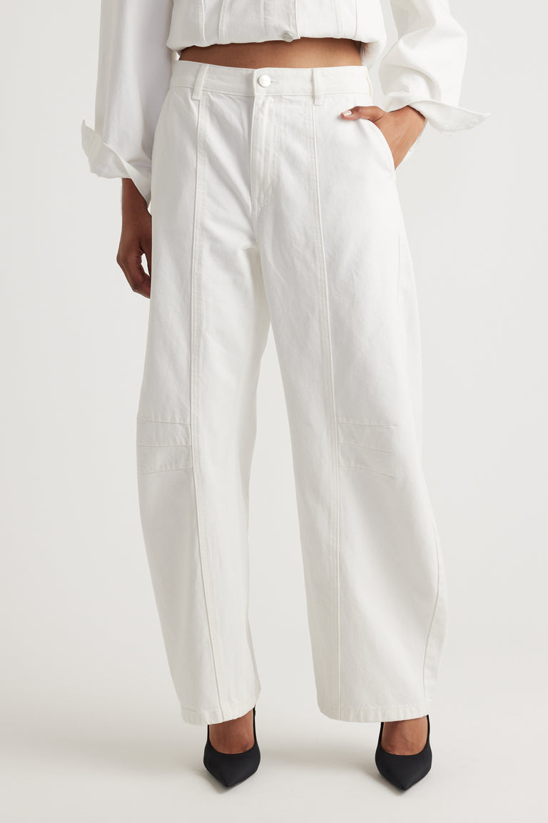 Person wearing white barrel jeans and a white top on a plain background