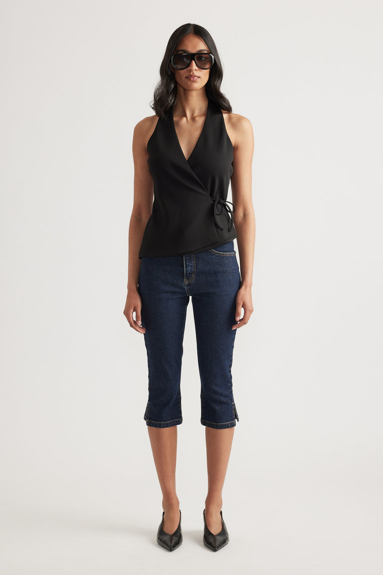 Woman wearing a black sleeveless wrap top with side tie, dark cropped jeans, sunglasses and pointed heels